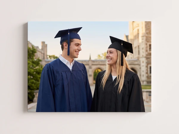 Canvas print of two graduates in navy and black gowns smiling at each other on campus