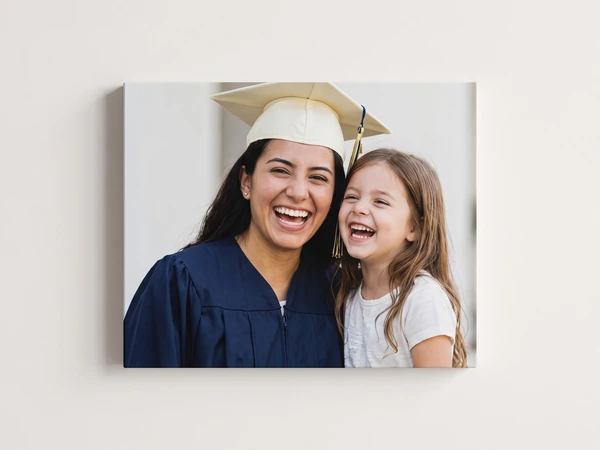 Canvas print of a laughing graduate in a cream cap with her little sister