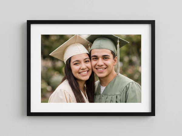 Black framed print of two graduates in cream and sage caps cheek to cheek