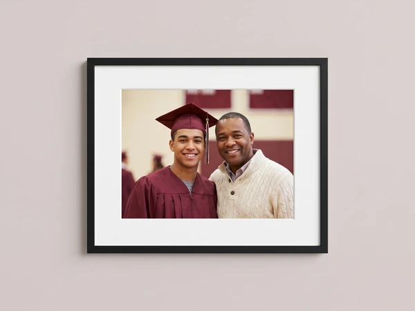 Black framed print of a graduate in a maroon gown with his father