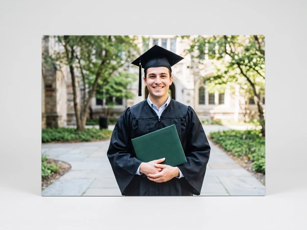 Metal print of a graduate holding a green diploma cover on a garden path