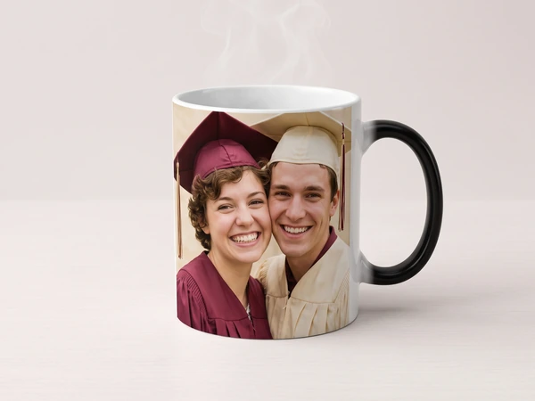 Magic mug with a black handle and steam rising, printed with two graduates cheek to cheek