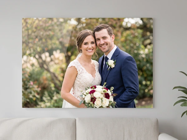 Acrylic print of a bride with a red and white bouquet beside her groom, above a sofa
