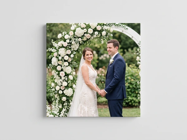 Square canvas print of a bride and groom holding hands under a white flower arch