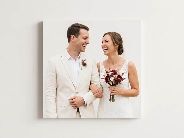 Square canvas print of a laughing couple, the groom in a cream suit and the bride holding burgundy flowers