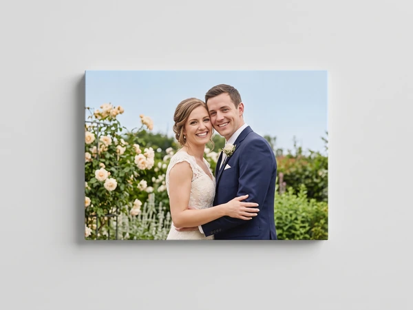 Landscape canvas print of a bride and groom embracing beside a climbing rose bush