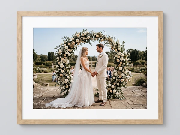 Light oak framed print of a couple holding hands under a round floral arch