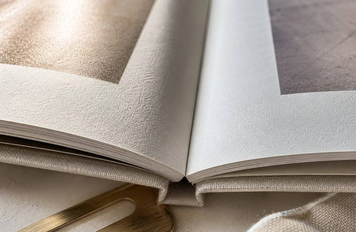 Close-up of open photo book pages showing premium paper texture and the binding detail at the spine