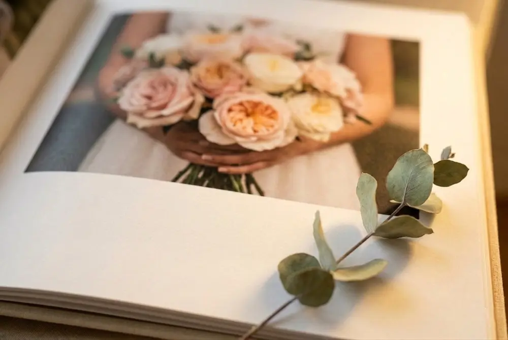 Open layflat wedding photo book showing ceremony and reception images on a wooden table with dried flowers