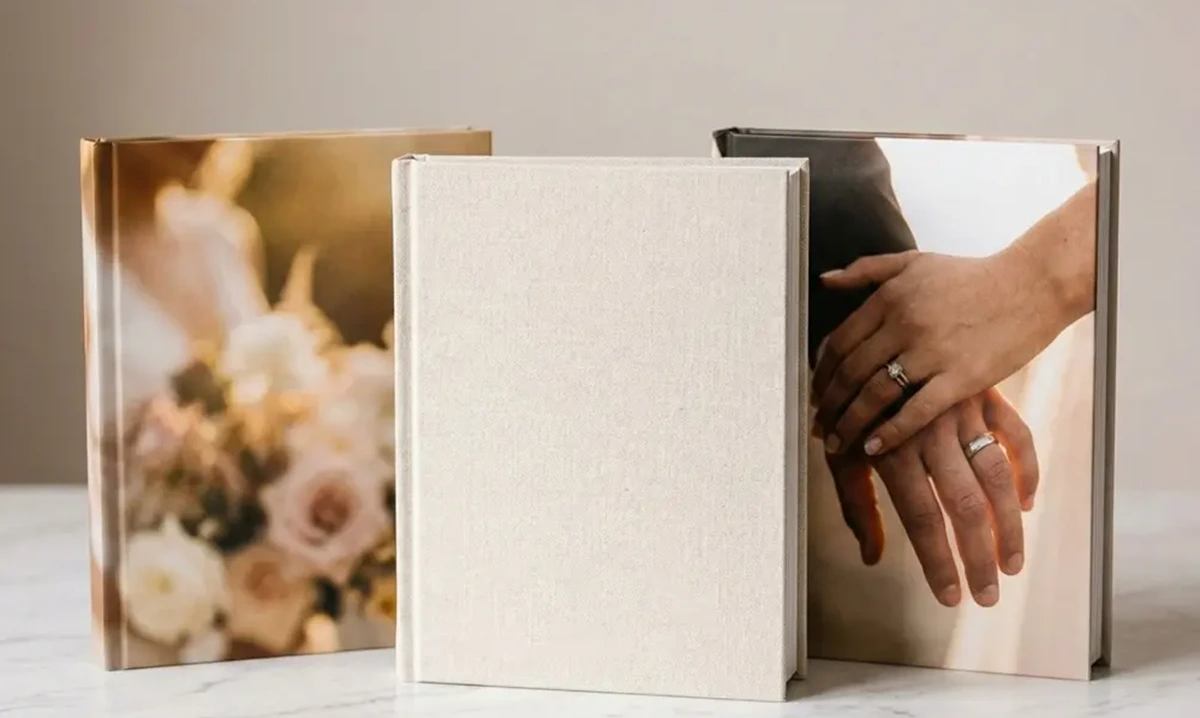Close-up of an elegant hardcover wedding photo book cover with embossed text on a linen surface
