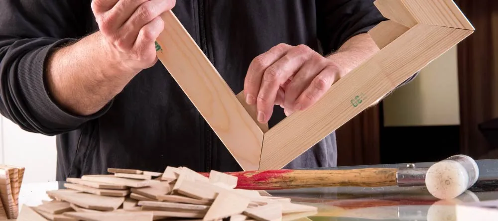 How to frame a rolled canvas print. Man inserting wedge in canvas stretcher frame.