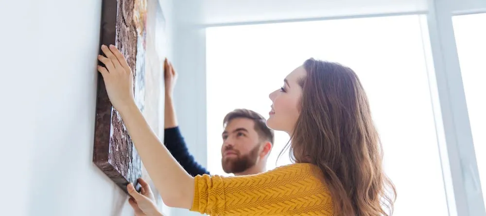10 Common Myths About Personalized Canvas Prints: Part II. Young couple hanging canvas photo print on wall.