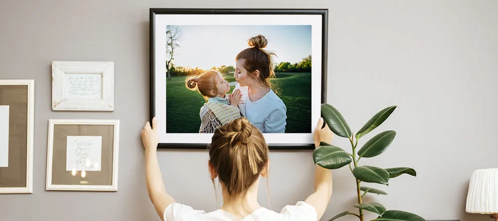 How to Make a Gallery Wall – Follow These 6 Steps. Woman hanging a framed photo print.