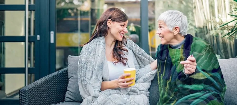 How to Wash a Photo Blanket at Home. Young woman having conversation with her mom while wrapped in blanket.