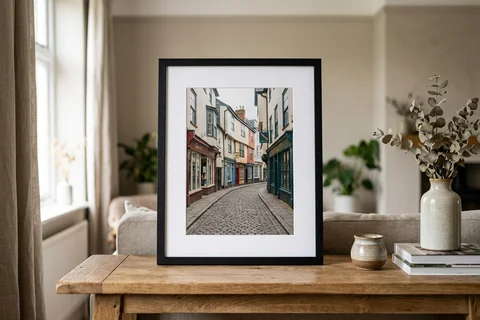 framed photo print exeter – a framed print of Gandy Street with a white mount and black frame standing on a console table