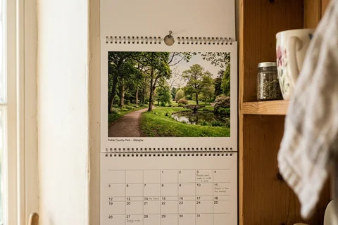 photo calendar glasgow – a spiral-bound wall calendar open on a month showing Pollok Country Park, hanging in a kitchen