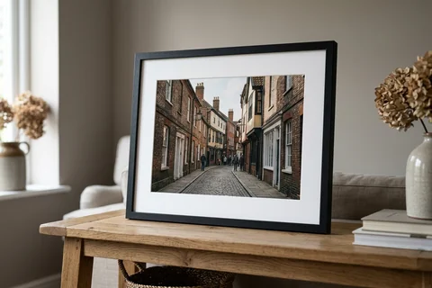 framed photo print norwich – a framed print of the Norwich Lanes with a white mount and black frame standing on a console table