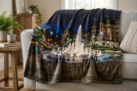 photo blanket sheffield – a plush blanket printed edge to edge with the Peace Gardens fountains at night draped over a sofa