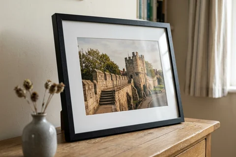 framed photo print york – a framed print of the city walls at Micklegate Bar with a white mount and black frame standing on a console table