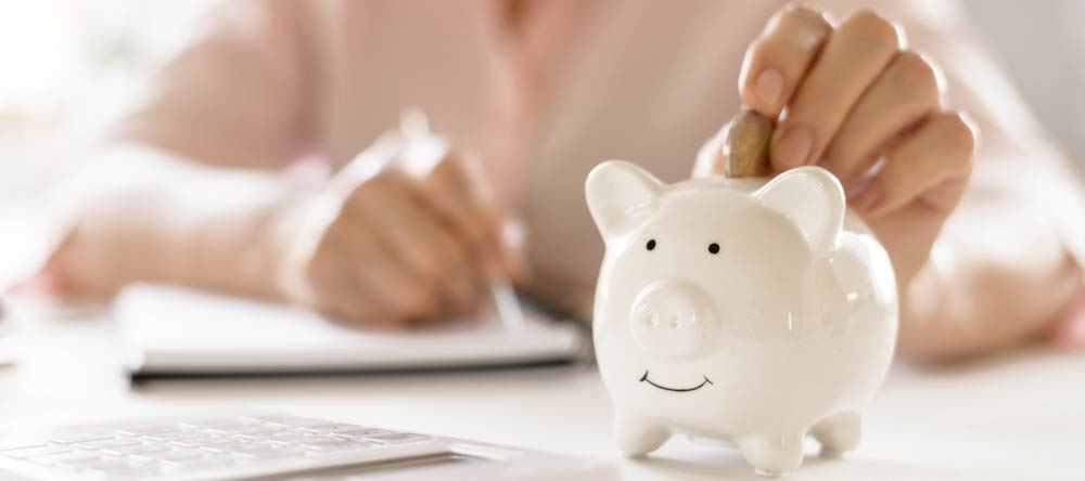 Where to Print Pictures Near Me. Woman calculating her budget with piggy bank next to her.